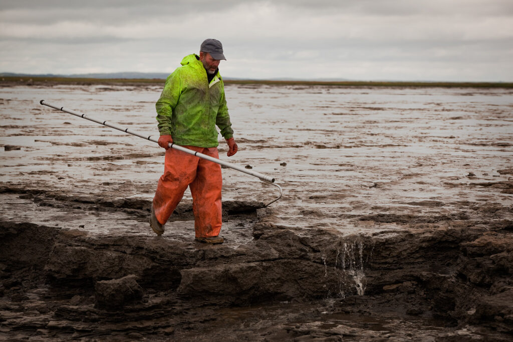 Man carrying a boat hook at low tide